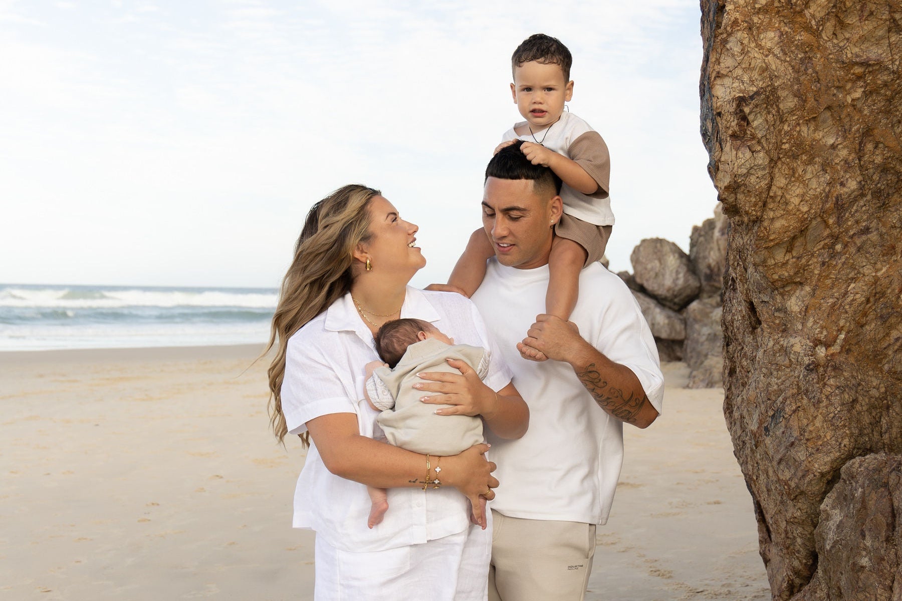 Family of four on a beach with large rocks and ocean in the background