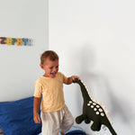 Child playing with a dinosaur toy on a bed in a room with colorful letters on the wall.