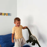 Child playing with a dinosaur toy on a bed in a room with colorful letters on the wall.