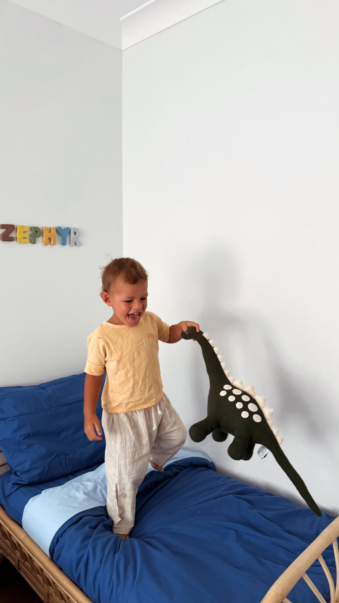 Child playing with a dinosaur toy on a bed in a room with colorful letters on the wall.
