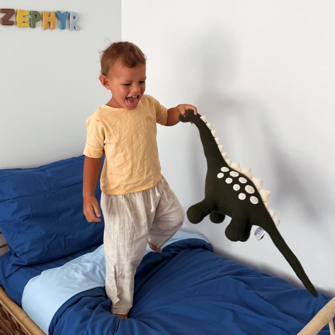 Child playing with a dinosaur toy on a bed in a room with colorful letters on the wall.