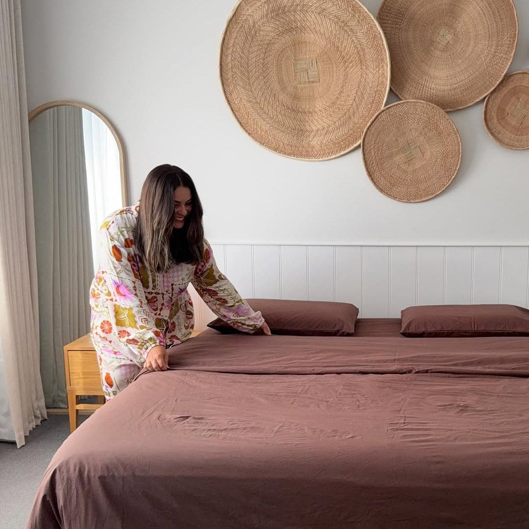 Woman arranging bedding in a bedroom with decorative wall plates.