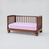 Wooden crib with a pink mattress on a white background