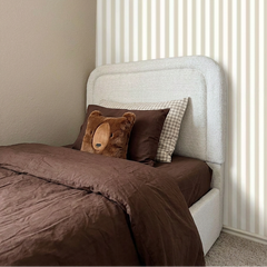 Bed with brown bedding and a teddy bear pillow against a white headboard.