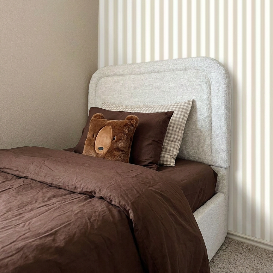 Bed with brown bedding and a teddy bear pillow against a white headboard.