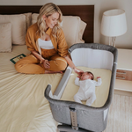 Woman sitting on a bed next to a baby in a bassinet