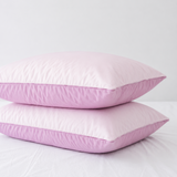 Two light pink pillows stacked on a white bed against a white background.