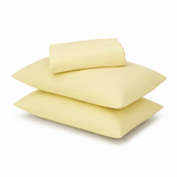 Three pale yellow pillows and a matching folded sheet or pillowcase stacked on a white background.