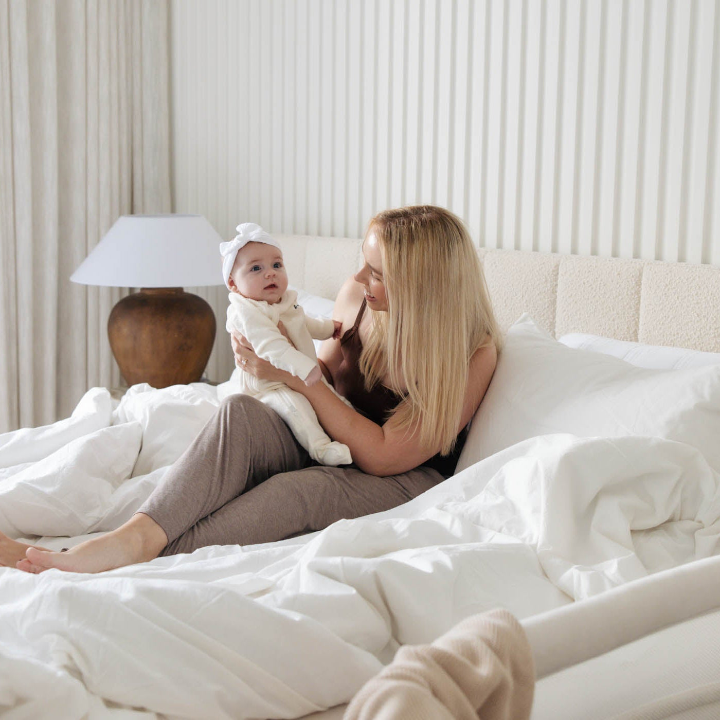 Woman holding a baby on a bed in a bright bedroom