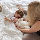 Woman and two children lying on a bed with a baby doll