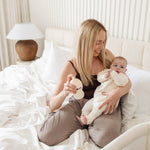 Woman holding a baby and a teddy bear in a bedroom setting