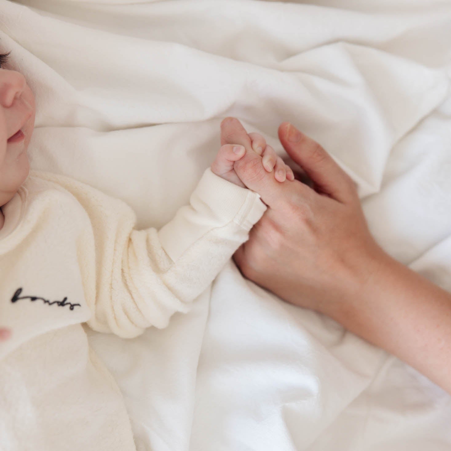 Newborn baby's hand held by an adult's hand under a white blanket