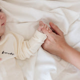 Newborn baby's hand held by an adult's hand under a white blanket