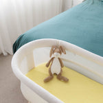 Baby crib with a yellow mattress and plush toy in a room with a bed and curtains.