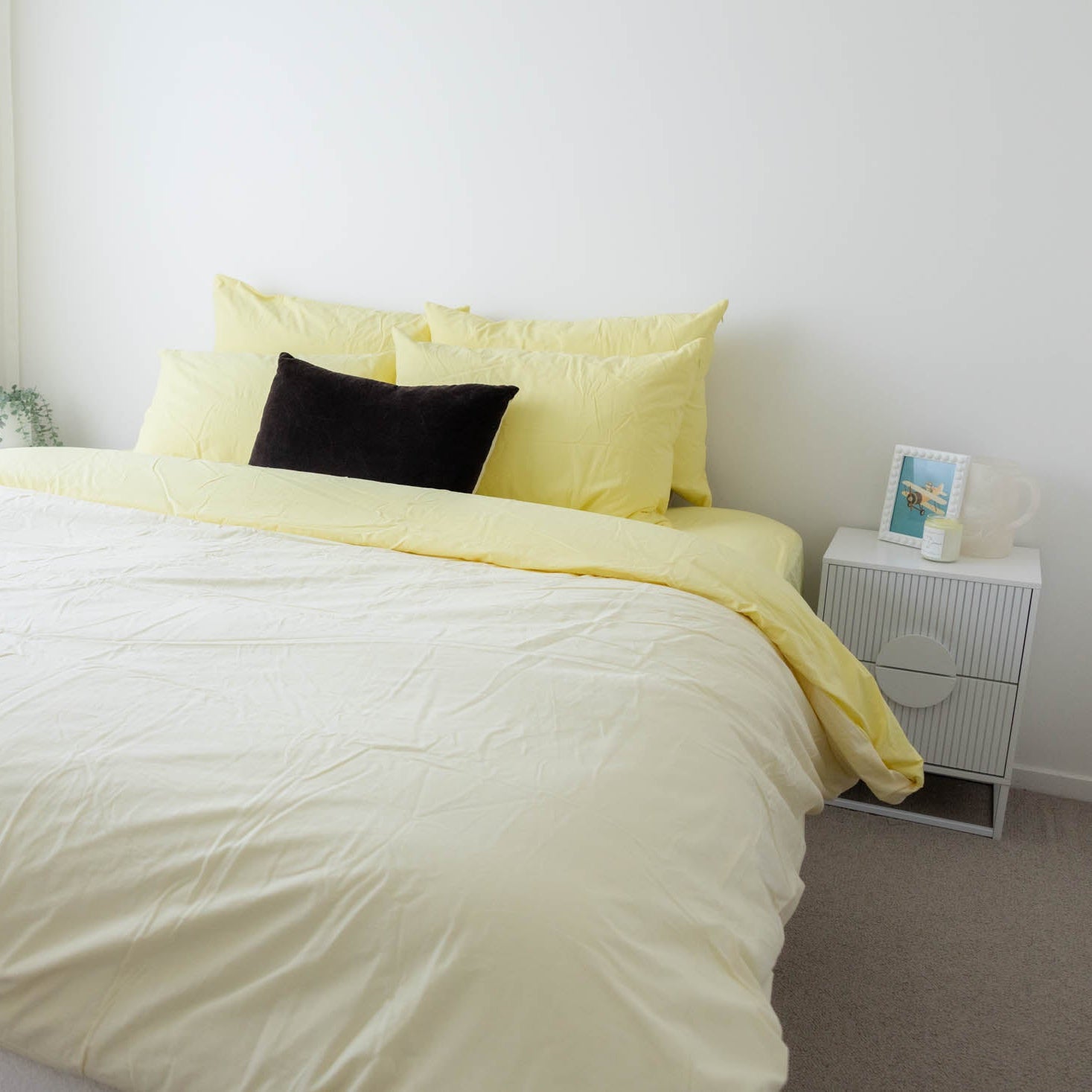 Bed with yellow bedding and black pillow in a minimalistic bedroom.