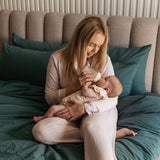 Woman holding a baby on a bed with green bedding and a beige headboard.