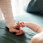 Baby's hand reaching towards an adult's hand on a bed