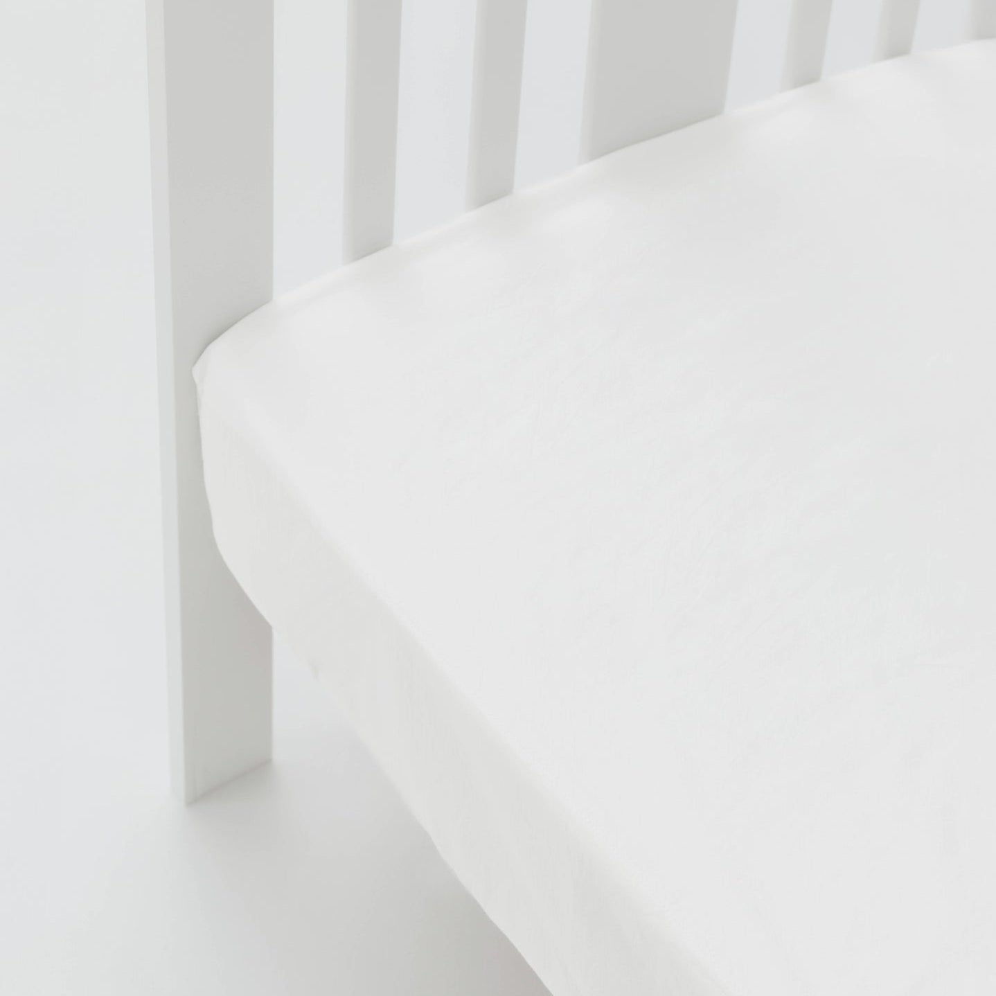 White crib with a fitted sheet on a white background