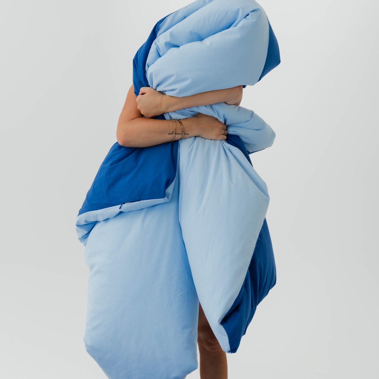 Person wrapped in a blue blanket against a light gray background