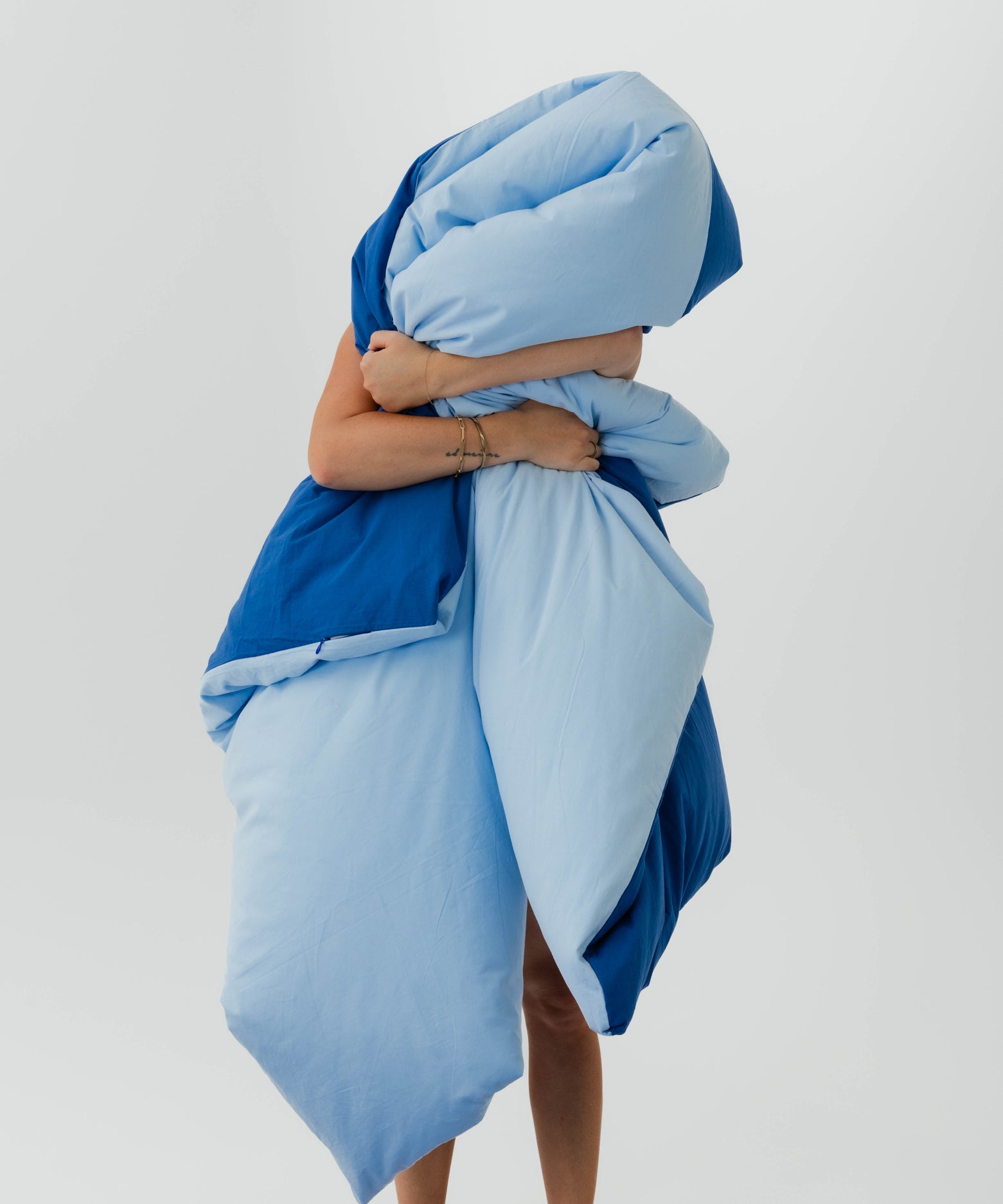 Person wrapped in a blue blanket against a light gray background