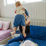 Woman holding a child on a bed with a colorful toy in a room.