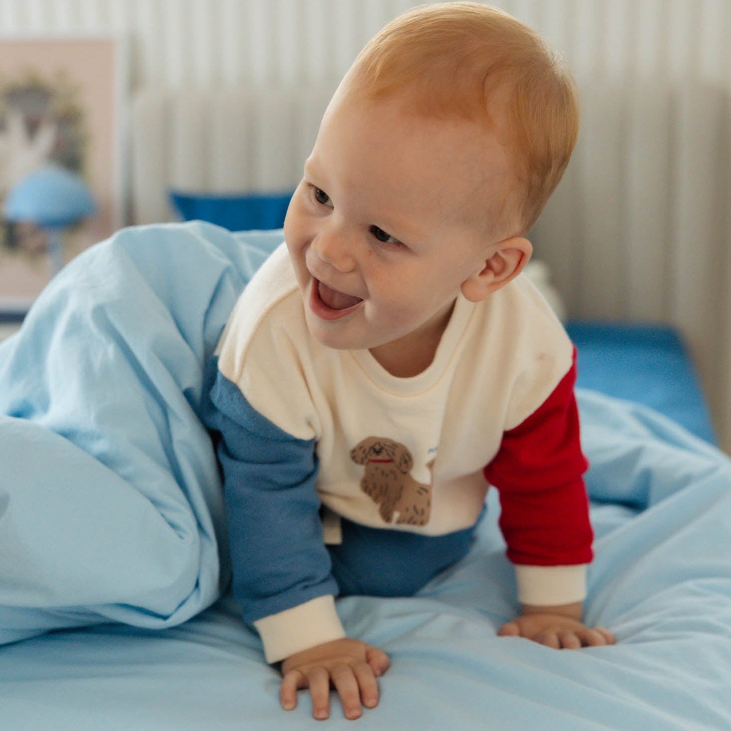 Baby in a red and white outfit with blue sleeves sitting on a light blue blanket.