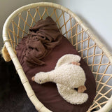 Wicker crib with brown blanket and white plush toy on a dark surface.