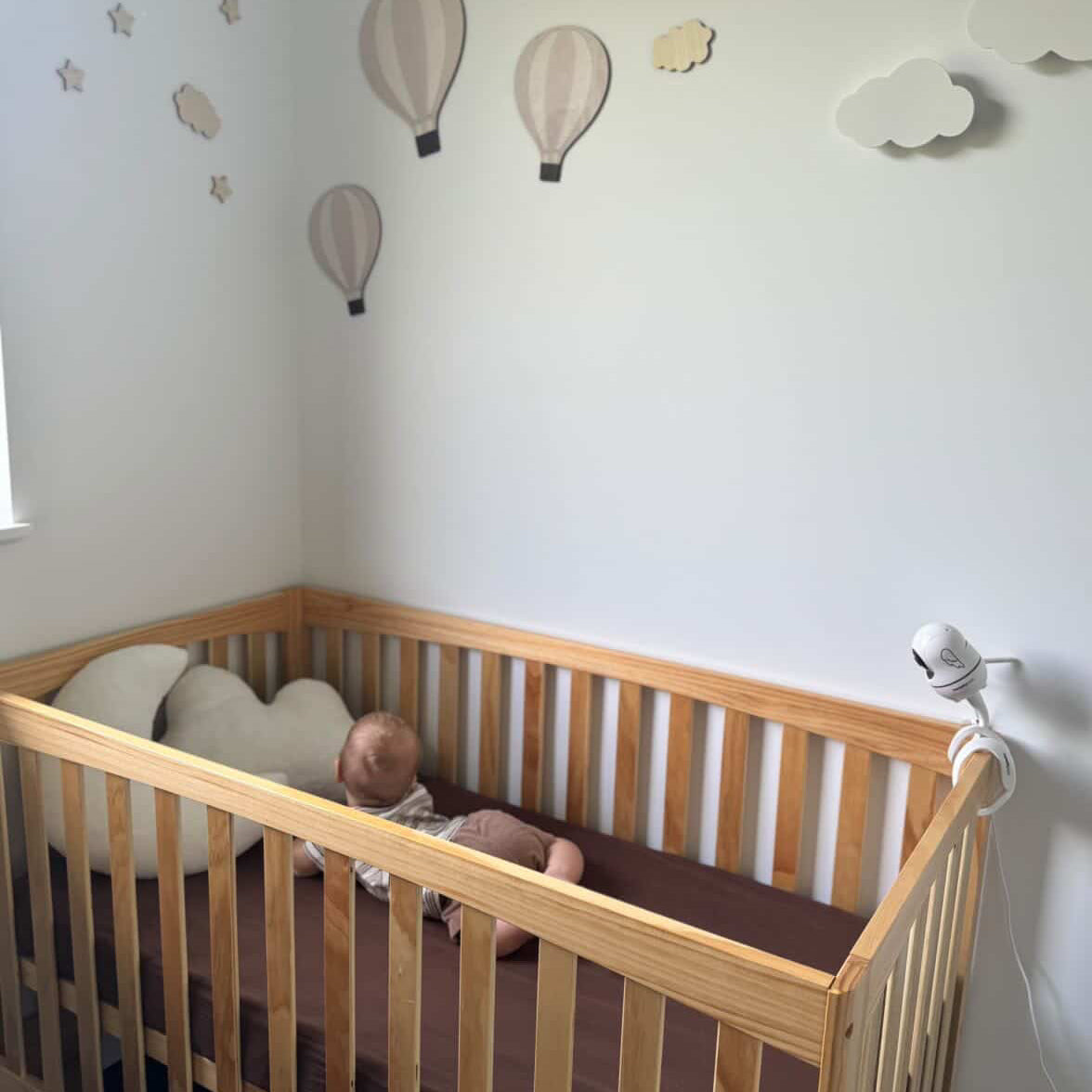 Baby in a wooden crib with decorative hot air balloons on the wall