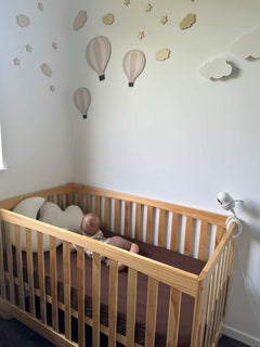 Baby in a wooden crib with decorative hot air balloons on the wall
