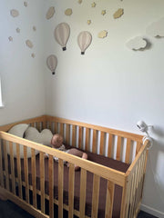 Baby in a wooden crib with decorative hot air balloons on the wall