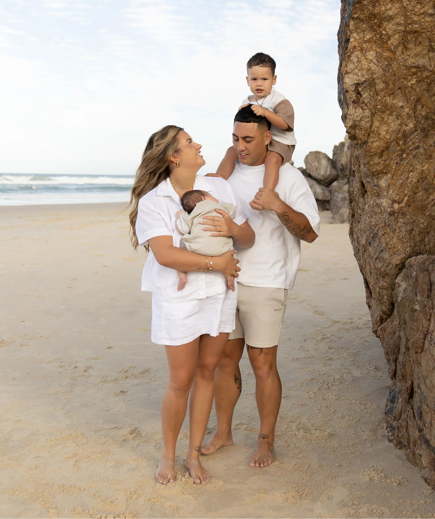 Family of three on a beach with large rocks and ocean in the background